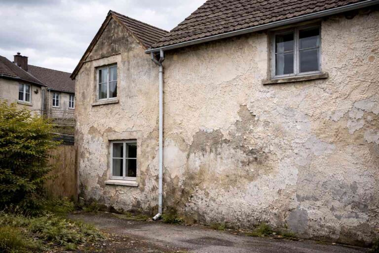 Old residential house with peeling exterior wall coating and damp stains